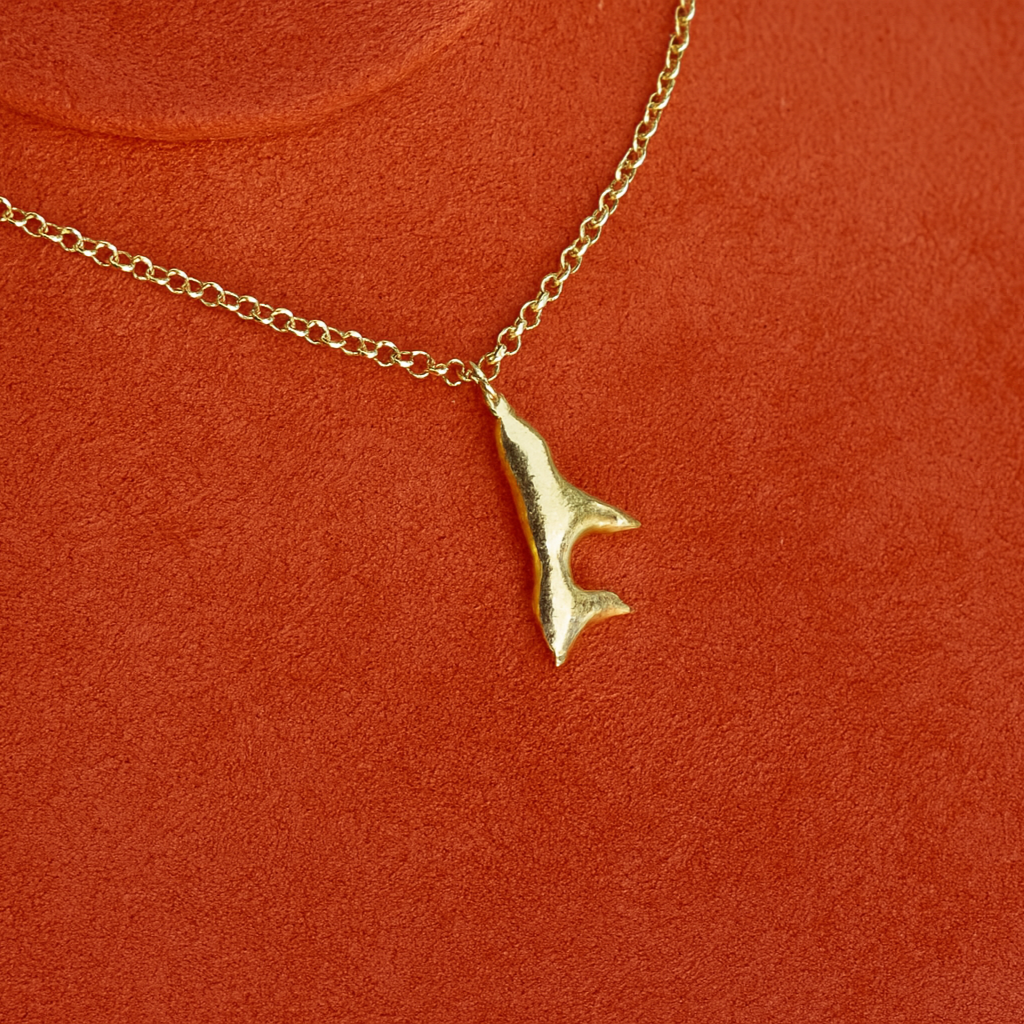 Gold necklace with a unique pendant on an orange surface