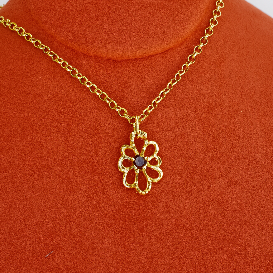 Gold necklace with a flower pendant on an orange stand.