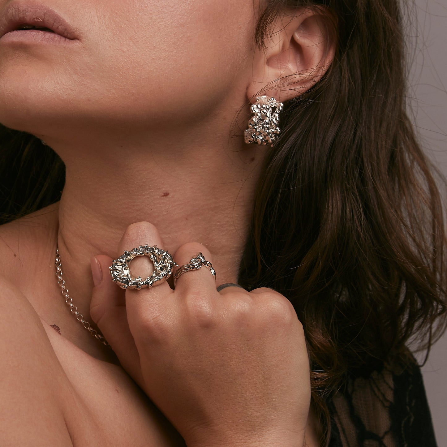 Close-up of a person wearing silver jewelry including earrings, rings, and a bracelet.