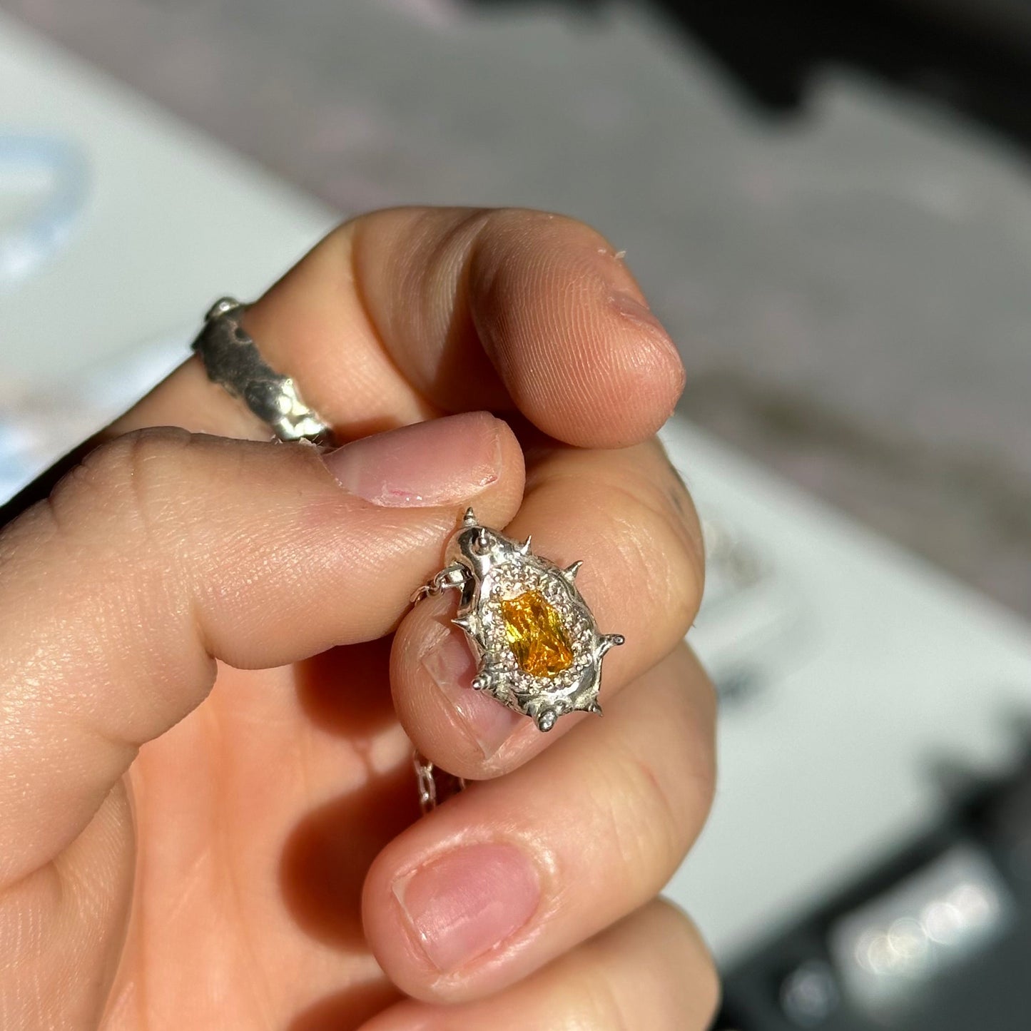 Hand holding a silver ring with a yellow gemstone against a blurred background