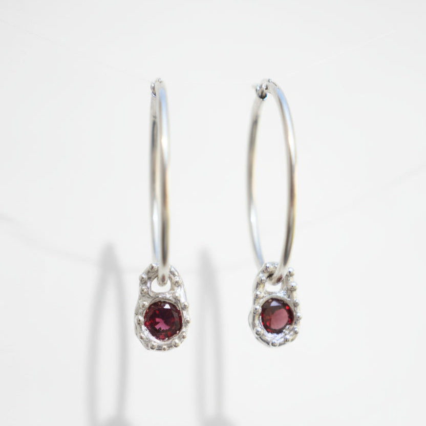 Silver hoop earrings with red gemstones on a white background